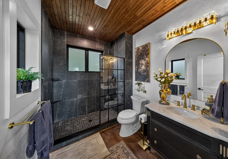 The bath with a black-framed glass walk-in shower and brass vanity lights